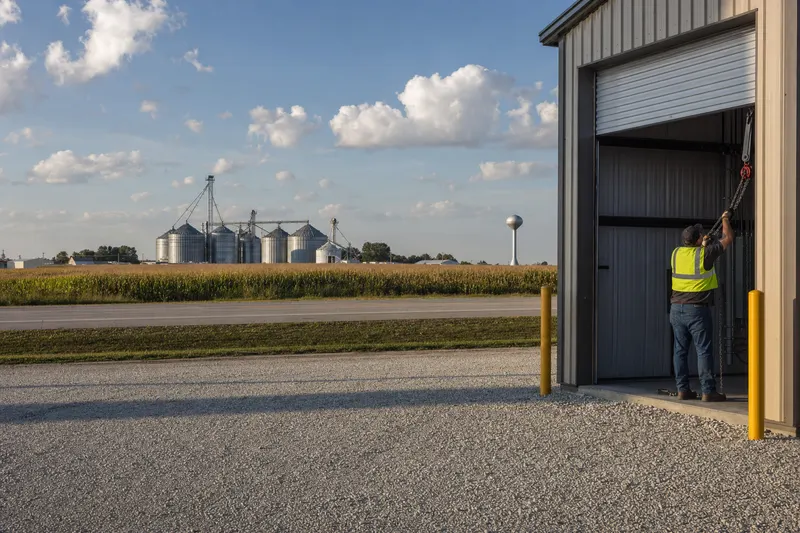 Technician inspecting the chain hoist of a rolling steel door on a metal warehouse near grain bins